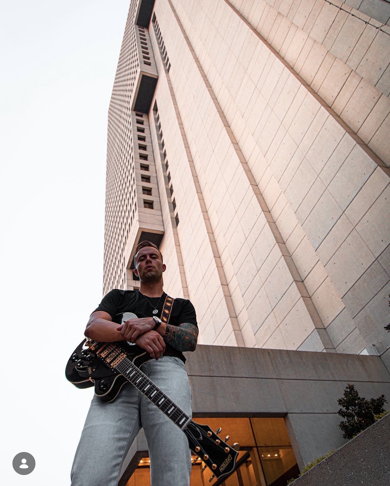 Tom Lail with a black electric guitar in front of a downtown high-rise