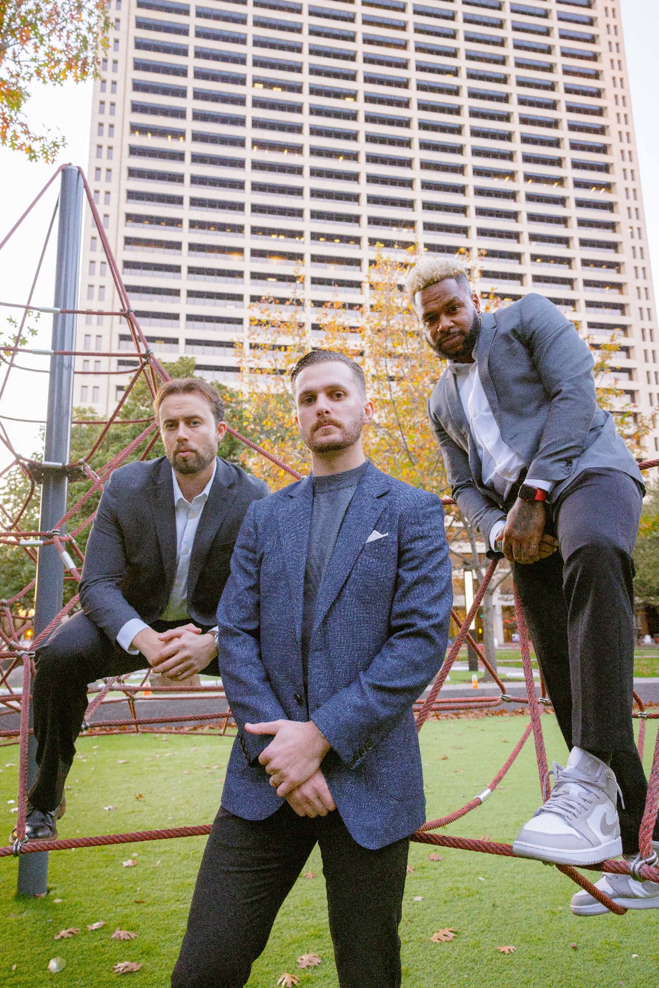 Three TrueGuard property managers in blazers posing on a red rope climbing structure in front of a downtown high-rise