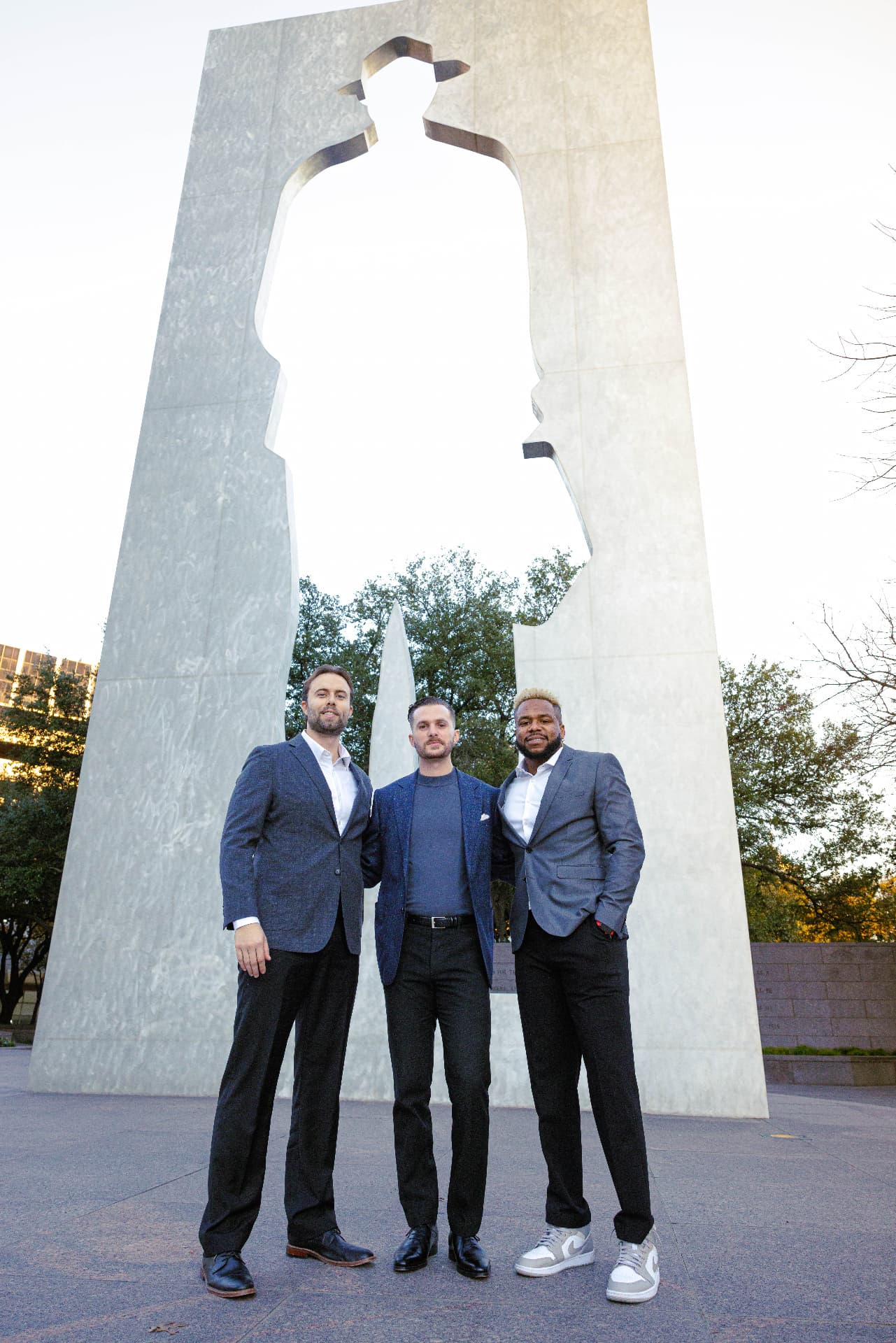 Three TrueGuard property managers in blazers standing in front of a stone monument on a paved plaza