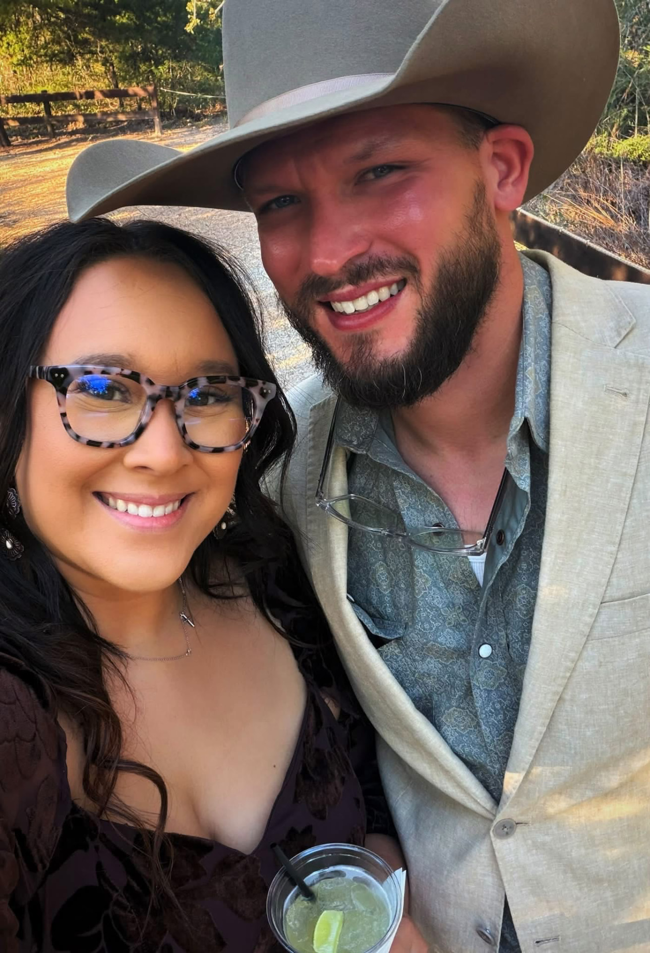 Cody in a cowboy hat and light blazer smiling beside a woman outdoors