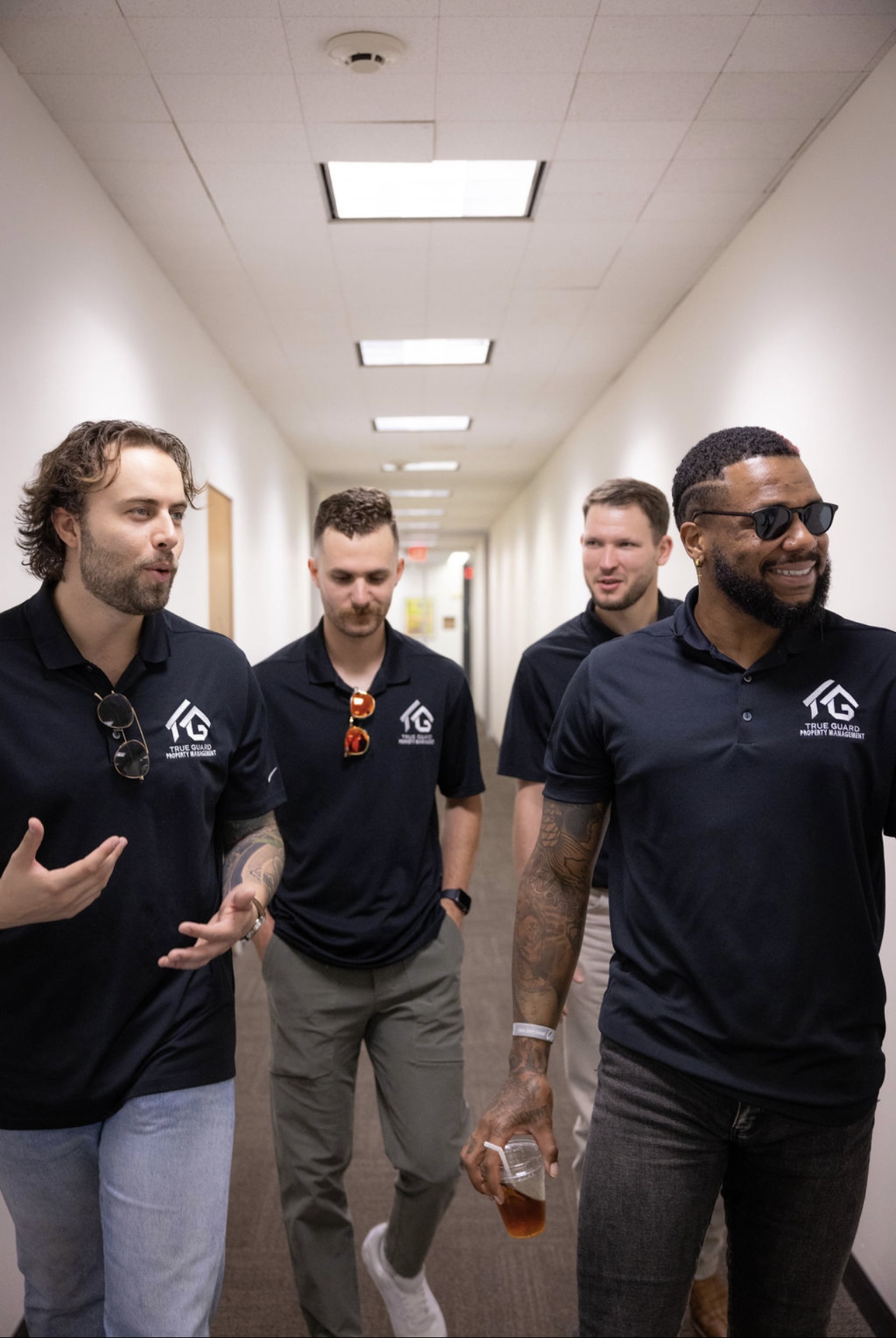Four TrueGuard property managers in black TrueGuard polo shirts walking together down an office hallway