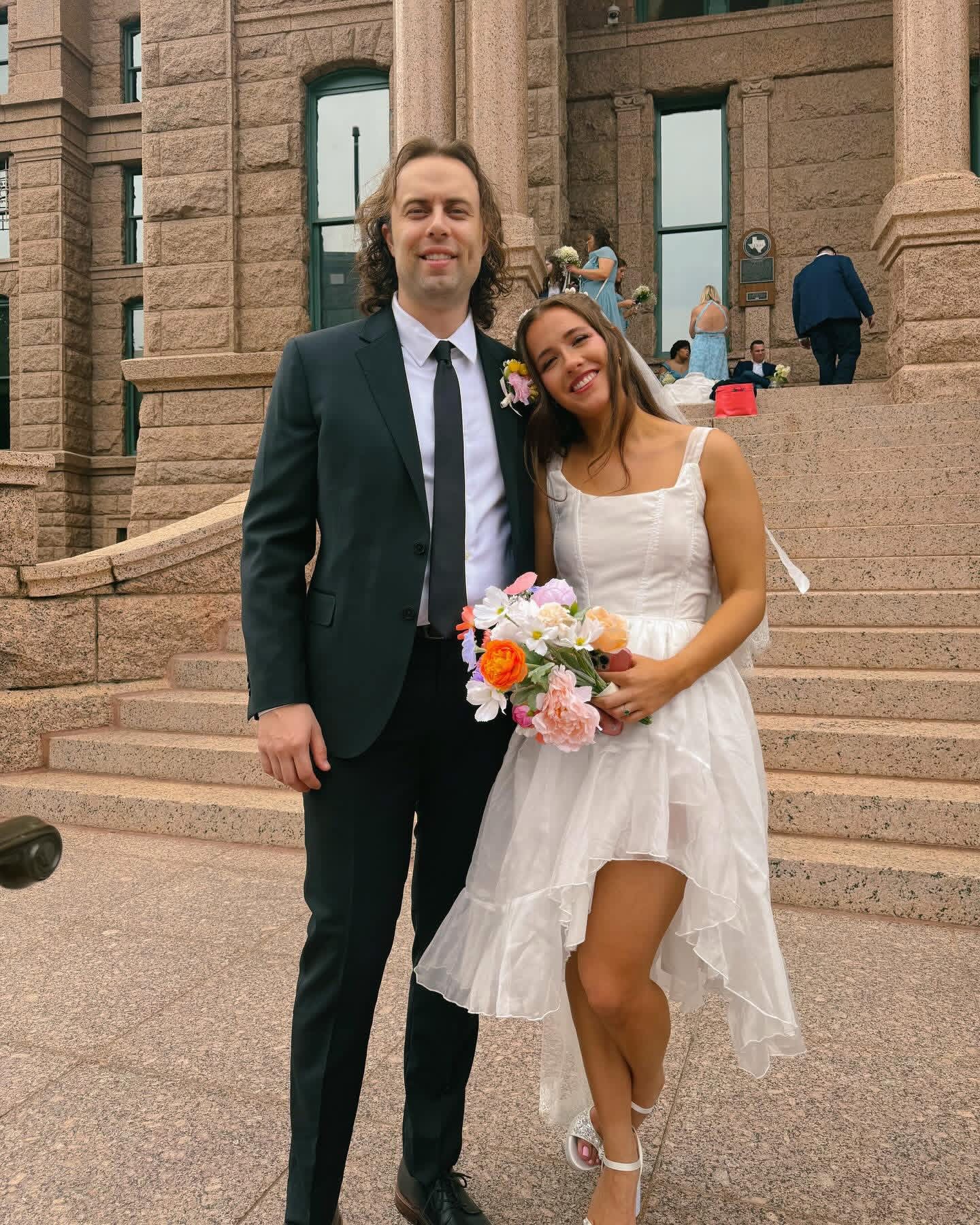 Tom Lail and his wife in wedding attire on the granite steps of the Texas State Capitol